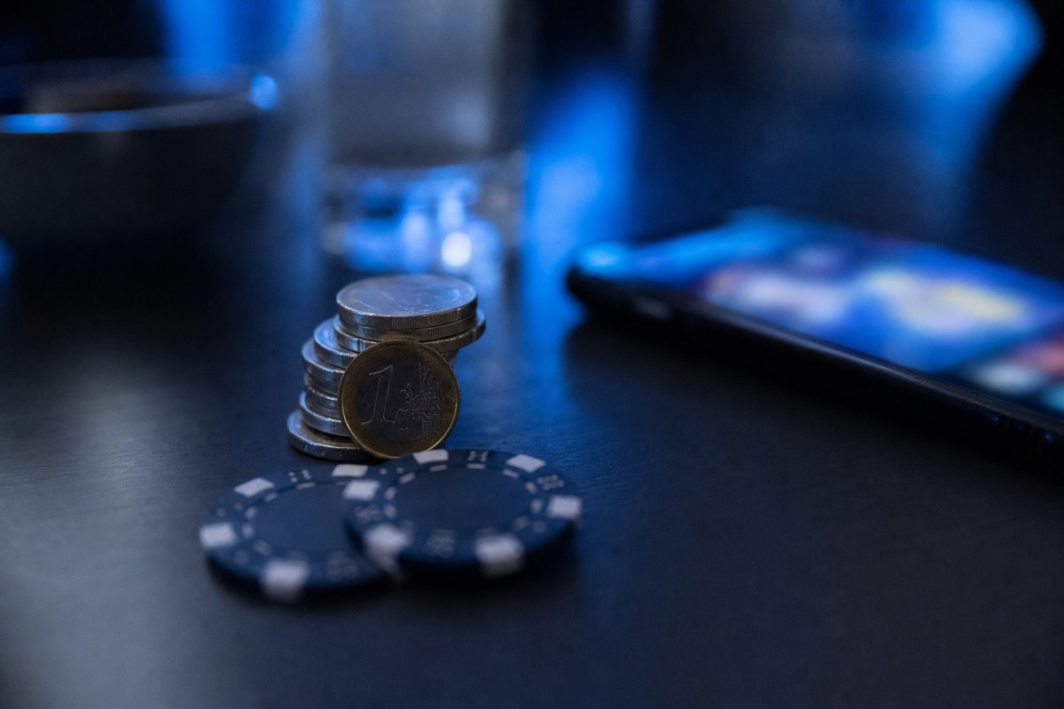 Münzstapel und Chips neben einem Smartphone mit abstraktem Slot-Spiel